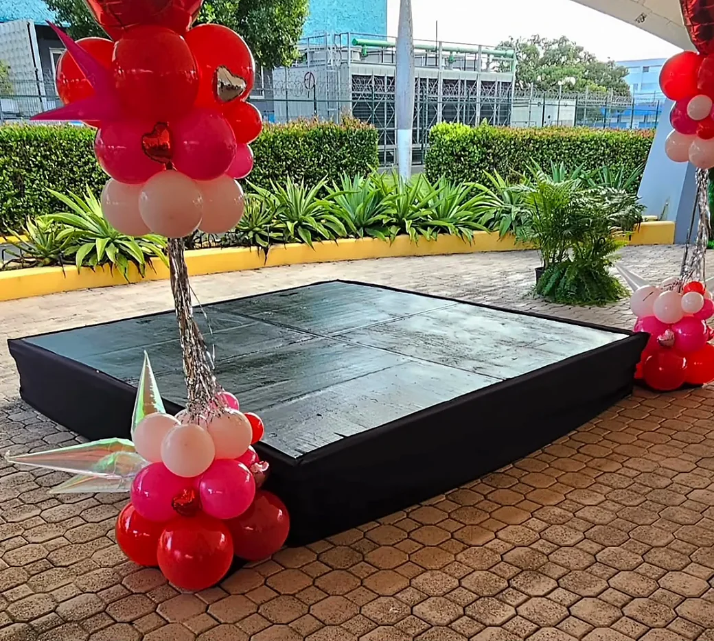 Tarima negra de cuatro secciones montada en un patio de losa con columnas de globos
